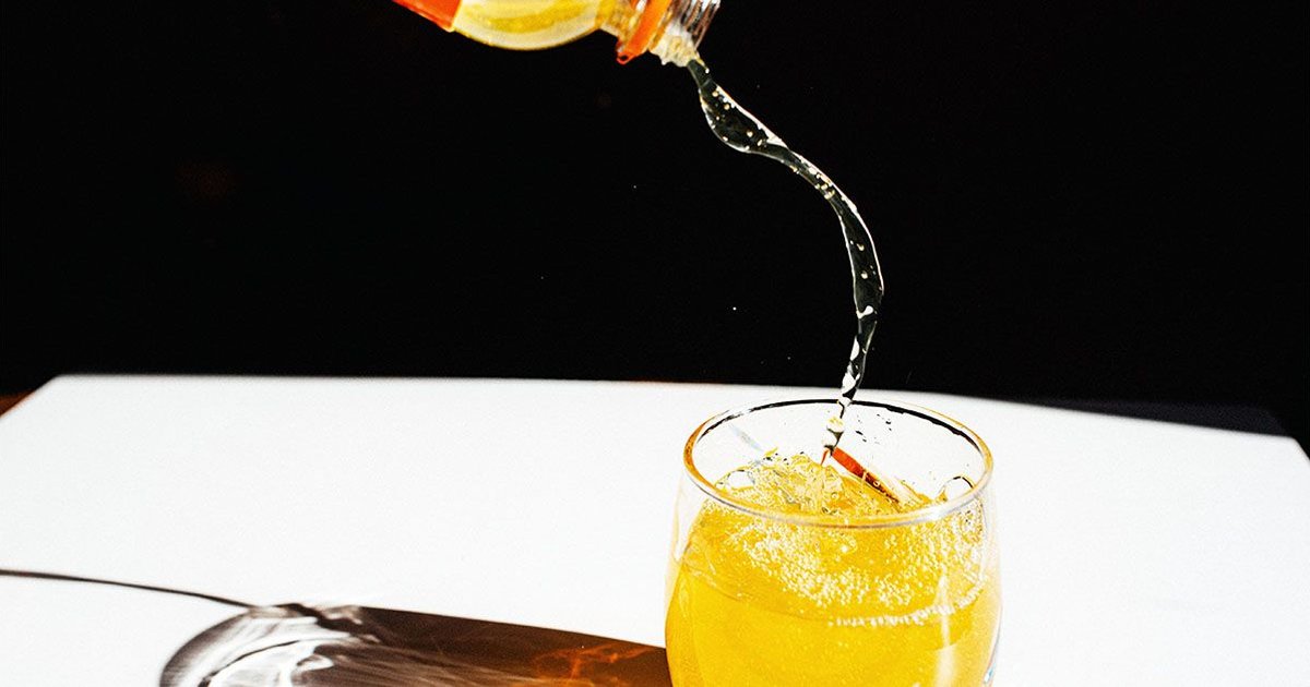 A glass of orange liquid being poured, representing artificial sweeteners in beverages.