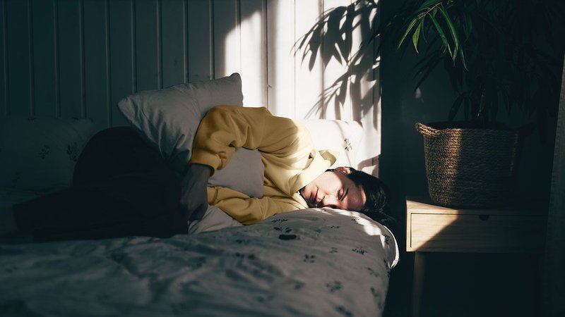 Person laying on their side on a bed holding their stomach