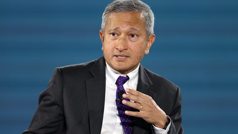 Vivian Balakrishnan, wearing a suit and in front of a blue backdrop, speaks and gestures with his hand.