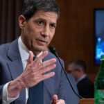 Kevin Warsh speaking at a financial conference, analyzing Fed policies and stock market impacts.