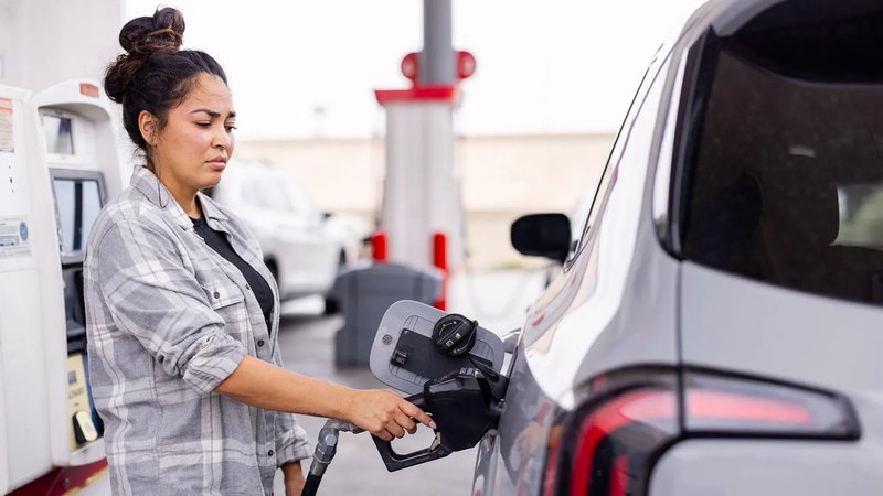Getty Images A woman in a grey checked shirt fills up a car at a petrol station.