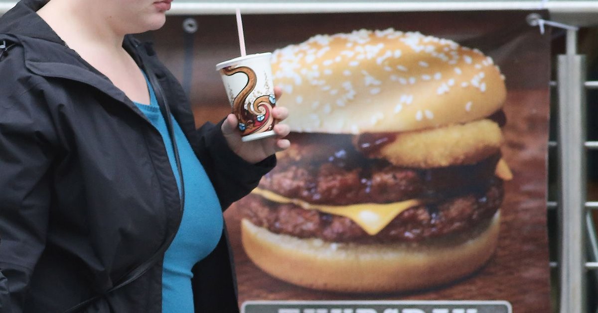 Person walking past a sign advertising a hamburger, highlighting ultraprocessed food risks